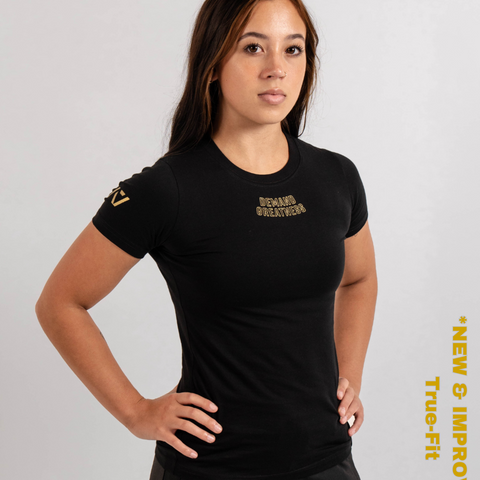 Woman wearing A7's IPF Approved Gold Meet shirt. 'Demand Greatness’ written on the front of black meet t-shirt in a gold double outlined font to have impact on the competition platform. Paired with black powerlifting joggers made from a stretchy material to use in strength sports training. 