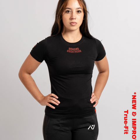 Woman wearing A7's IPF Approved Red Dawn Meet shirt. 'Demand Greatness’ written on the front of black meet t-shirt in a red double outlined font to have impact on the competition platform. Paired with black powerlifting joggers made from a stretchy material to use in strength sports training. 