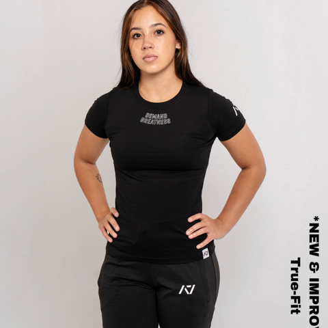 Woman wearing A7's IPF Approved domino Meet shirt. 'Demand Greatness’ written on the front of black meet t-shirt in a white double outlined font to have impact on the competition platform. Paired with black powerlifting joggers made from a stretchy material to use in strength sports training. 