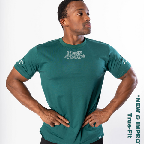 Man wearing A7's IPF Approved Emerald Foras Meet shirt. 'Demand Greatness’ written on the front of green meet t-shirt in a white double outlined font to have impact on the competition platform. Paired with black powerlifting shorts made from a stretchy squat proof material to use in strength sports training. 
