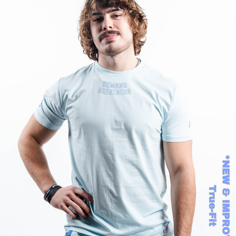 Man wearing A7's IPF Approved Cyanite light blue Meet shirt. 'Demand Greatness’ written on the front in a blue double outlined font to have impact on the competition platform. Paired with light blue powerlifting shorts made from a stretchy squat proof material to use in strength sports training.