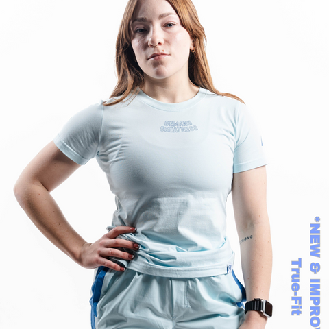 Woman wearing A7's IPF Approved Cyanite light blue Meet shirt. 'Demand Greatness’ written on the front in a blue double outlined font to have impact on the competition platform. Paired with light blue powerlifting shorts made from a stretchy squat proof material to use in strength sports training.
